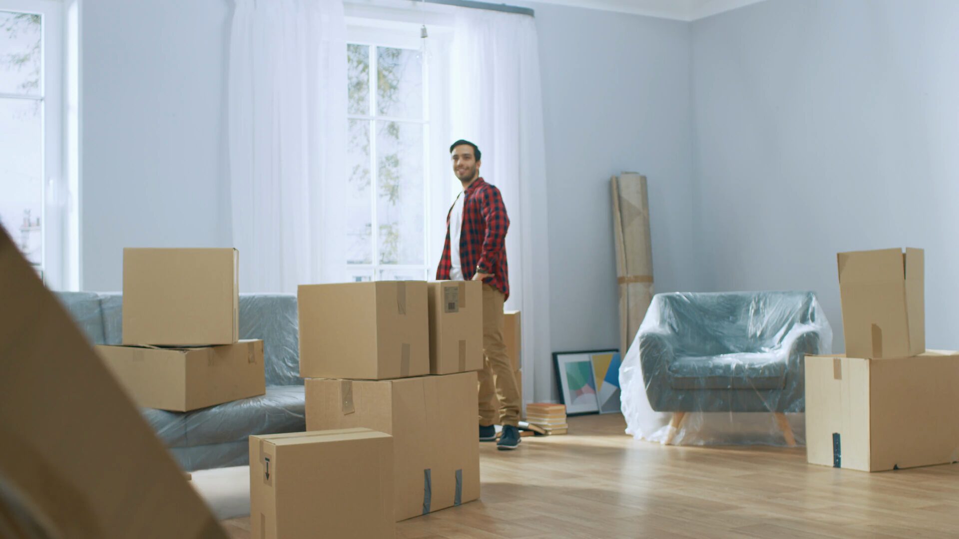 Movers carrying cartons through the living room of a home being packed, furniture wrapped and boxes stacked